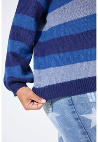 Maglione lavorato a maglia con strisce orizzontali in blu, navy e grigio. Presenta polsini e orlo a coste. Mano appoggiata sul bordo inferiore.