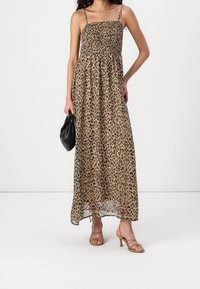 Leopard print maxi dress with smocked bodice, thin straps, and flowing fabric. Paired with strappy tan heels and a black clutch bag.