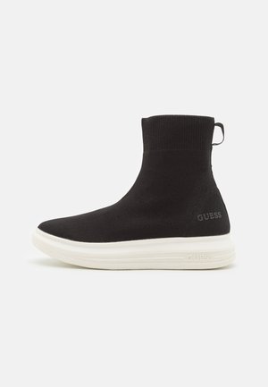 Schwarzer Sneaker-Boot im Stricksocken-Design mit weißer dicker Sohle, Zuglasche an der Ferse und "GUESS"-Logo an der Seite und auf der Sohle.