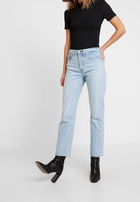 Vaqueros de mezclilla azul claro con corte recto y cintura alta, combinados con una blusa negra ajustada y botines negros de tacón.