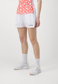 White sporty shorts with a smooth texture and a black "HEAD" logo on the side, paired with white sneakers and ankle socks.