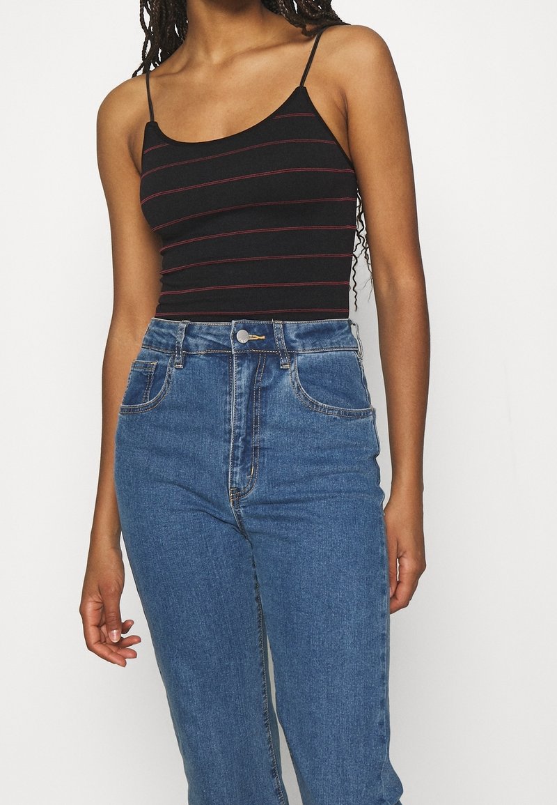 Débardeur noir à rayures horizontales rouges, fabriqué en tissu extensible, associé à un jean bleu taille haute avec fermeture éclair et bouton.