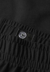 Zwarte stof met een elastische tailleband en een geplooid textuur, ontworpen voor comfort en pasvorm, met een transparante knopdetail.