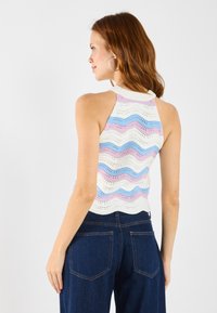 Adīta halter tops ar viļņotu rakstu pasteļu krāsās (rozā, zila, balta), ar ribotu apkakli, kombinēta ar tumšiem džinsiem.