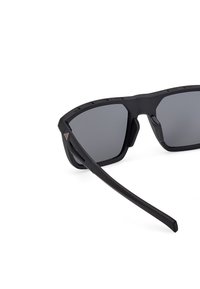 Ochelari de soare negri cu lentile gri, design cu ramă unghiulară, accente din cauciuc texturat și brațe laterale late. Material din policarbonat ușor.