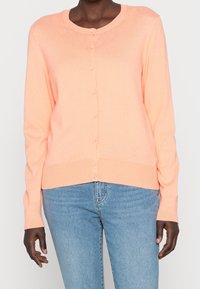 Persikofärgad kofta i mjukt tyg, med rund halsringning, långa ärmar och full knäppning fram. Ribbad kant och manschetter.