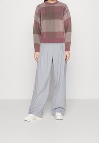 Pull gris, mauve et beige avec un motif à carreaux ; pantalon ample gris clair ; texture douce ; assorti à des baskets de couleur claire.