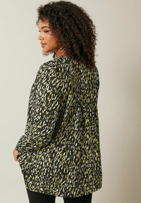 Blusa a maniche lunghe con un motivo astratto in nero, bianco e giallo, caratterizzata da una vestibilità comoda e dettagli di plissettatura sul retro.