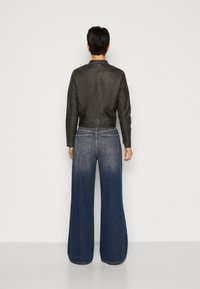Veste en cuir noir cropped avec un col simple, associée à un jean bleu à jambe large qui passe de foncé à clair en bas.