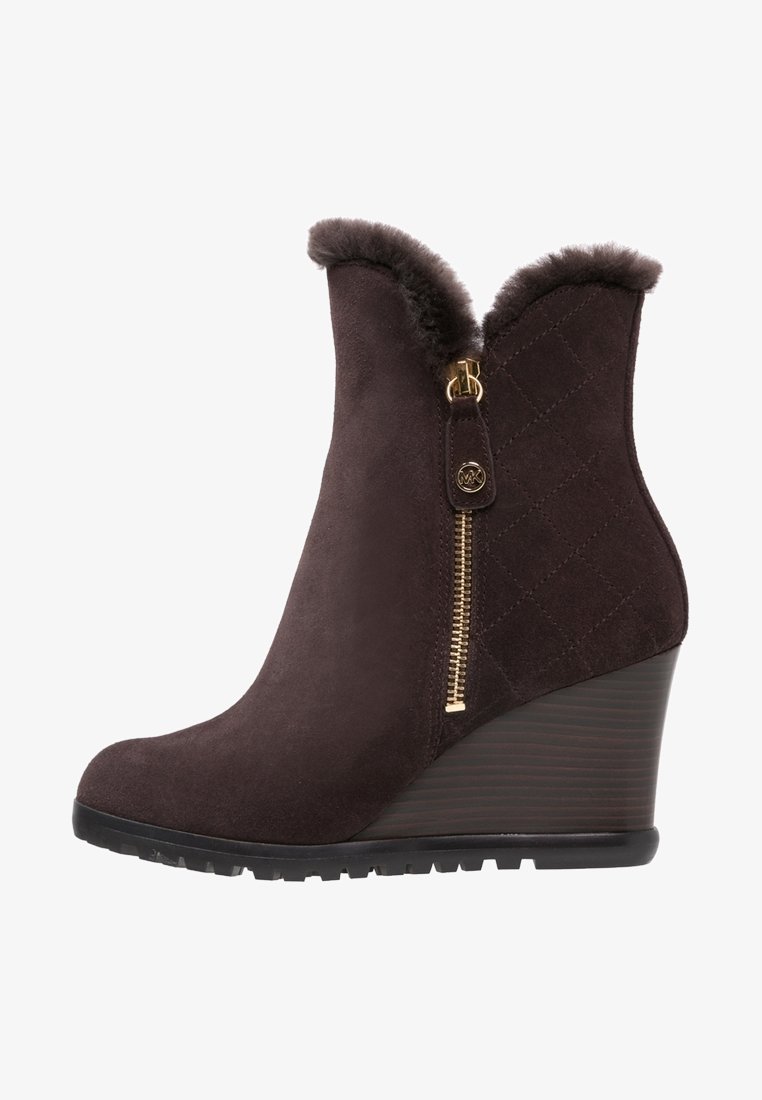 Hnědá semišová kotníková bota na klínu s umělým kožíškem na lemu, bočním zipem se zlatými kovovými doplňky a prošíváním na vrchní části a texturovanou podrážkou.