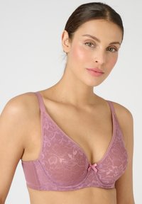 Reggiseno in pizzo di un rosa tenue con un motivo floreale, dotato di una fascia sottostante liscia e spalline regolabili, rifinito con un piccolo dettaglio in nastro al centro.