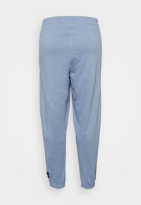 Calças de moletão azul claro com cintura elástica, tornozelos ajustados e um pequeno remendo de logótipo preto no lado esquerdo. Textura suave.