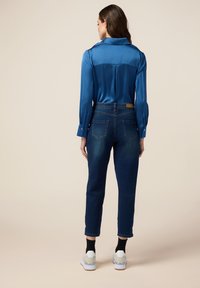 Camisa de satén azul de manga larga con cuello, combinada con jeans de color azul oscuro. El atuendo se completa con zapatillas gris y blancas.