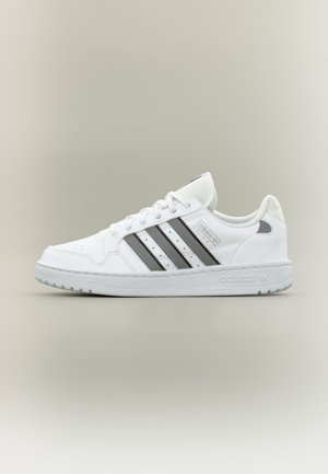 Weißer Adidas-Sneaker mit schwarzen Streifen, Schnürsenkeln und einer strukturierten Sohle, seitlich auf neutralem Hintergrund gezeigt.