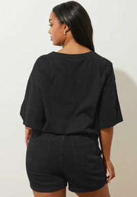 Musta ylisuuri t-paita lyhyillä hihoilla, yhdistettynä mustiin farkkushortseihin, joissa on kaksi takataskua ja kääritty helma. Silkkinen rakenne.