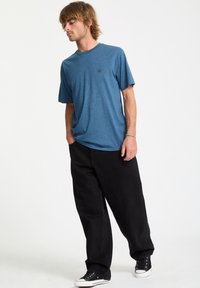 Kortærmet blå t-shirt med rund halsudskæring, parret med løstsiddende sorte jeans og sorte sneakers. Enkelt logo-detalje på trøjen.