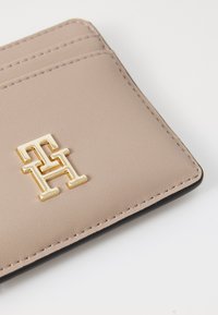 Beige leather cardholder featuring a gold-tone logo and multiple card slots, with precise stitching along the edges.