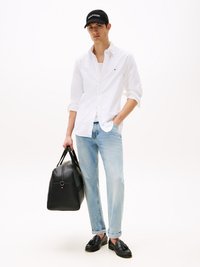 Camisa blanca de botones, vaqueros de lavado claro, bolso de cuero negro y mocasines negros. Gorra negra con el logo "TOMMY HILFIGER" en la parte delantera.