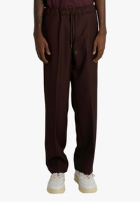 Pantaloni bordeaux a gamba larga con vita elasticizzata, coulisse e tessuto dalla texture liscia, abbinati a sneaker bianche.