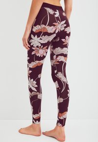 Legging met bloemmotief in donker bordeauxrood, met roze en crèmekleurige bloemen en groene accenten. Glad, rekbaar materiaal en aansluitend ontwerp.