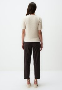Haut tricoté beige clair à manches courtes avec une texture douce, associé à un pantalon marron foncé. Les chaussures présentent un talon épais et des lanières à la cheville.