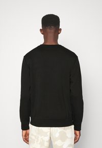 Svart crewneck sweatshirt med långa ärmar, av bomullsmaterial, ribbade ärmslut och nederkant, bärs över ljusa camobukser, som visar en solid bakvy.