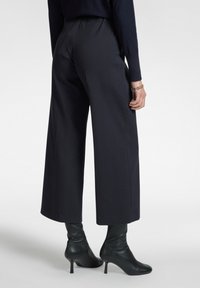 Brede broek in een donkere stof met een subtiel patroon. Elastische tailleband met een gladde textuur, gecombineerd met kniehoge zwarte laarzen.