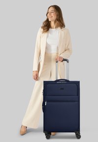 Valigia a rotelle navy con superficie texturizzata, due tasche frontali, maniglia estraibile e quattro ruote per la manovrabilità.
