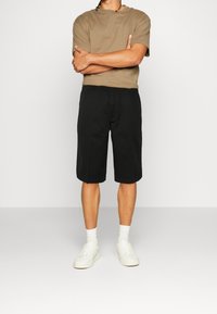 Hnědé tričko s krátkým rukávem spárované s černými šortkami ke kolenům a bílými teniskami. Jednoduchý design; jednobarevné bez vzorů.