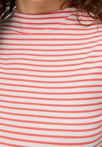 Randig ribbad topp i vitt med ljus korallfärgade ränder. Hög halsdesign med en figurnära passform och mjuk textur.
