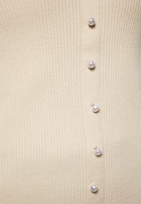 Pulover tricotat de culoare bej deschis, cu o textură ribbed, având cinci butoane decorativ din perlă de-a lungul plăcii frontale.