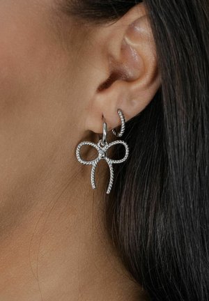 Silberne Creolen mit einer Schleifen-Design, aus gedrehtem Metall mit einer zentralen Perle gefertigt. Die Textur ist glatt mit detaillierten Akzenten.