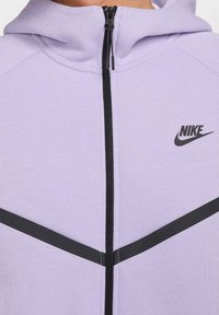 Felpa zip-up Nike viola con cerniera nera e dettagli neri, caratterizzata da design geometrici sulla parte anteriore. Realizzata in un morbido tessuto testurizzato.