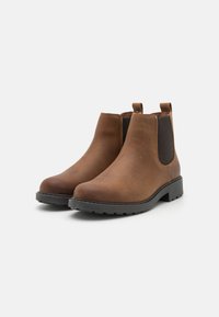 Botas de cuero marrón hasta el tobillo con un acabado suave, paneles laterales elásticos y una suela de goma negra gruesa. Presentan tiradores para un fácil calzado.