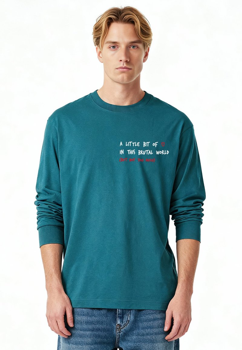 T-shirt à manches longues couleur sarcelle en coton, avec texte blanc et rouge affichant un message sur le devant. Col rond simple et coupe décontractée.