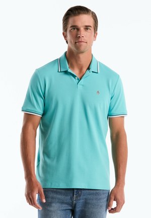 Mann trägt türkisfarbenes Poloshirt mit gestreiftem Kragen und Ärmeln, steht vor weißem Hintergrund.