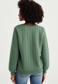 Grüner Strickpullover mit strukturiertem, erhabenem Zopfmuster, gerippten Bündchen und Saum. Verfügt über einen weiten Halsausschnitt und eine lockere Passform.