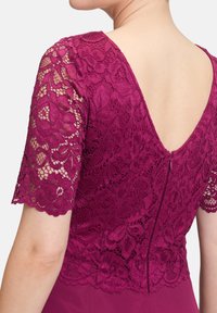 Robe bordeaux avec des manches courtes en dentelle florale et un dos en V profond, dotée d'une fermeture éclair discrète. La texture douce met en valeur les motifs complexes.