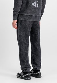 Dunkelgraue, strukturierte Sweatpants mit elastischen Bündchen, seitlichen Nähten und einem dezenten gewaschenen Effekt, kombiniert mit schwarzen Sportschuhen.