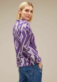 Maglione a motivo viola e grigio con un design geometrico, caratterizzato da un collo alto e una vestibilità comoda, abbinato a jeans in denim blu.