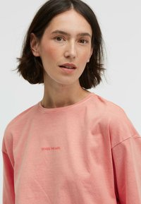 Weiches, rosa Baumwoll-T-Shirt mit rundem Halsausschnitt, lässiger Passform und gesticktem Text "SENSES. THE LABEL" auf der Brust. Glatte Textur.