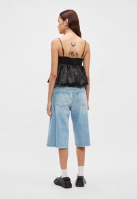 Czarny satynowy krótki top z marszczonym tyłem, zestawiony z jasnoniebieskimi spodniami culottes z denimu z surowym wykończeniem i bocznymi kieszeniami.