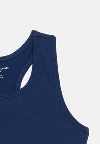 Μπλε ναυτικό μανίκωτο τοπ με φαρδιές τιράντες ώμων, ορατές ραφές και εσωτερική ετικέτα με κείμενο στο πάνω μέρος της πλάτης.