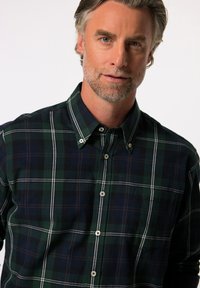 Camisa a cuadros verde y marino con cuello abotonado, que presenta líneas blancas y botones de plástico, fabricada con una textura de tela suave.