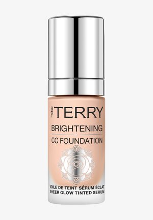 Bouteille pêche clair avec un capuchon pompe en argent, étiquetée "BY TERRY BRIGHTENING CC FOUNDATION." Présente un design de rose blanche décoratif.