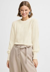 Pull crème avec un tricot texturé en motif losange, col rond et manches longues. Assorti avec un pantalon beige doté d'une ceinture nouée.