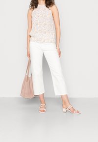 Blomstret halterneck-top i lyse pastelfarver, hvide cropped bukser, lyserød ruskinds-tote taske og lyserøde hælede sandaler.