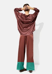 Brązowa bluzka w kropki o luźnym kroju, połączona z szerokimi spodniami z solidnym zielonym wykończeniem i podobnym wzorem w kropki.