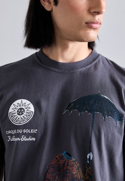 Gray cotton t-shirt featuring a circular sun logo and a multicolored graphic of a figure holding a dark umbrella. Short sleeves, crew neck design.