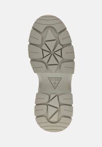 Suela de zapato en goma gris claro con un patrón de banda de rodadura angular, superficie texturizada y logotipo centrado dentro de un diseño triangular.